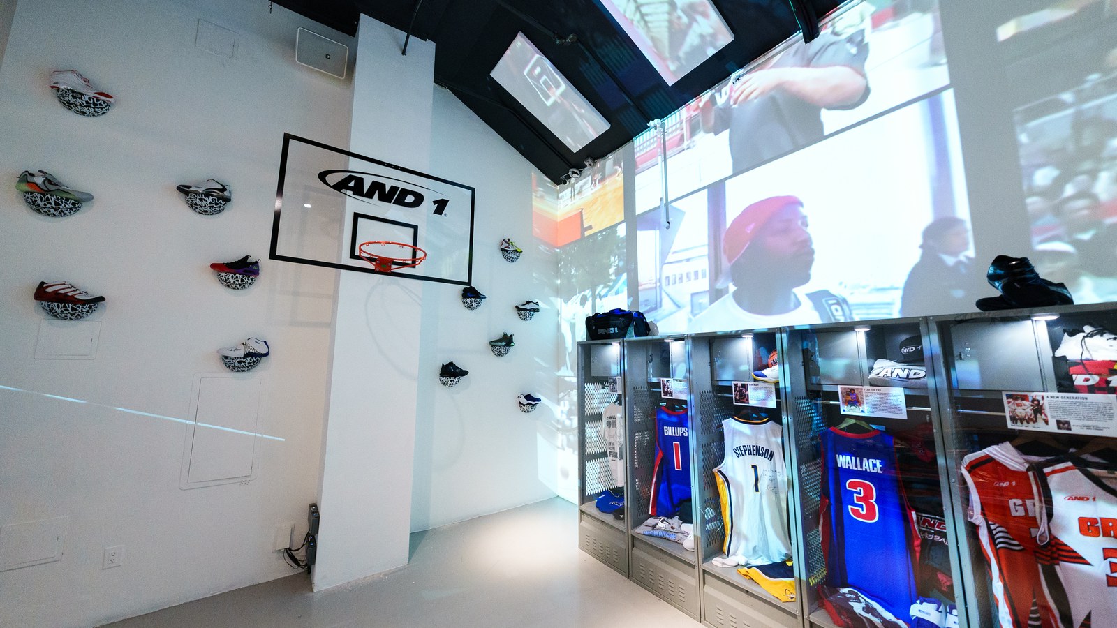Mini basketball hoop with AND1 logo on a white wall beside mounted sneakers and lit jersey lockers