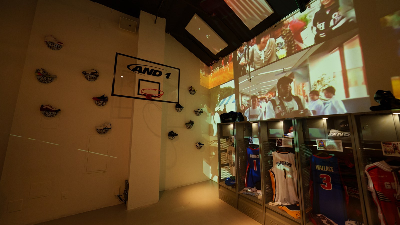AND1 hoop backboard on a wall of mounted sneakers, jersey lockers below a wide projection of a crowd