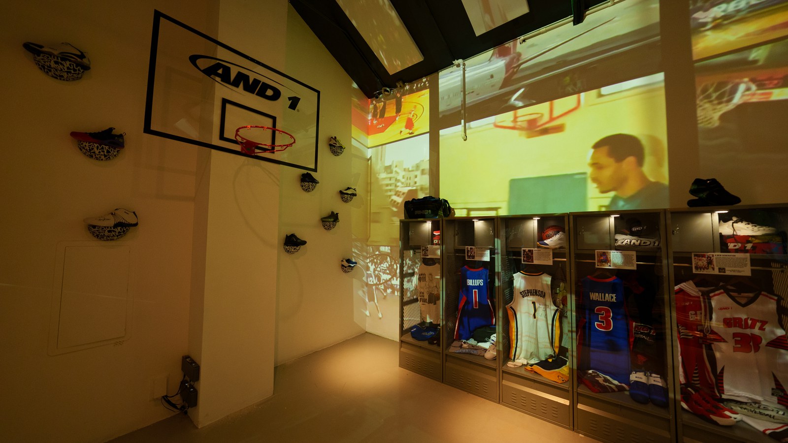 AND1 branded hoop, sneakers on a wall, and locker cases beneath a projected wall of game highlights