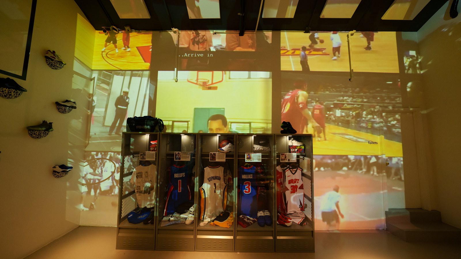 Jerseys in lit display lockers under a wall of projected yellow tinted basketball footage