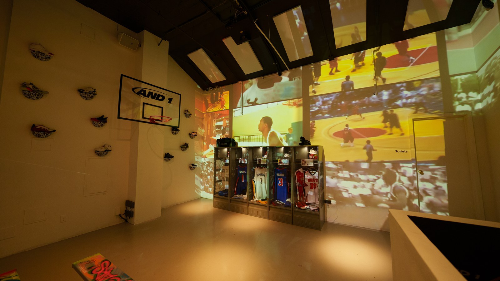 White showroom with an AND1 backboard, sneakers on the wall and basketball footage projected behind jersey lockers