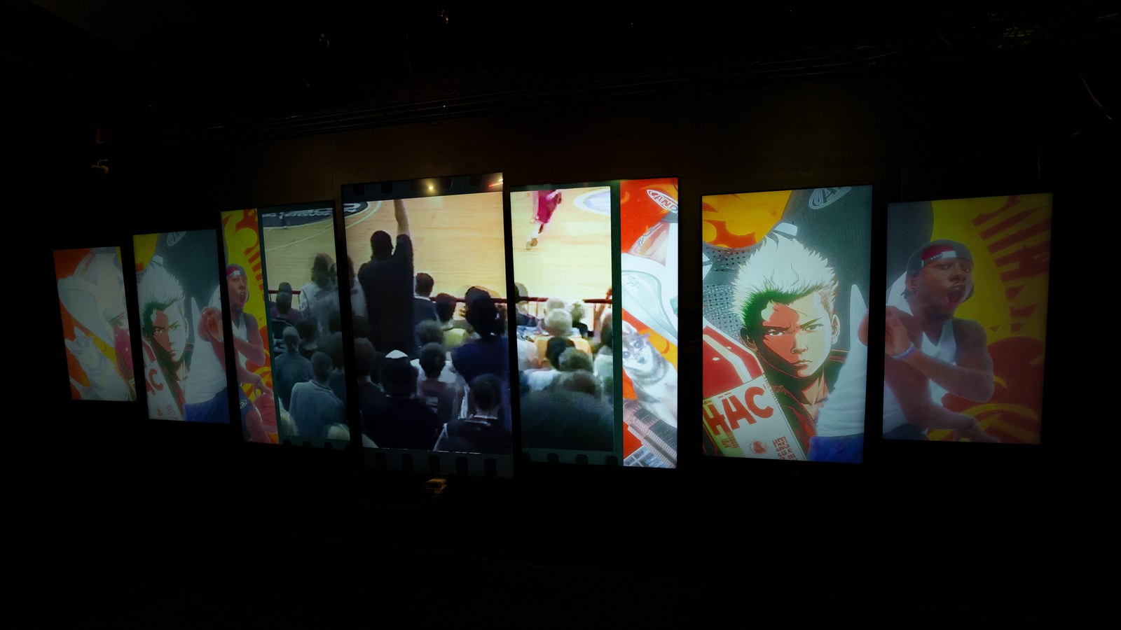 Row of tall vertical screens glowing with basketball and crowd footage in a dark room