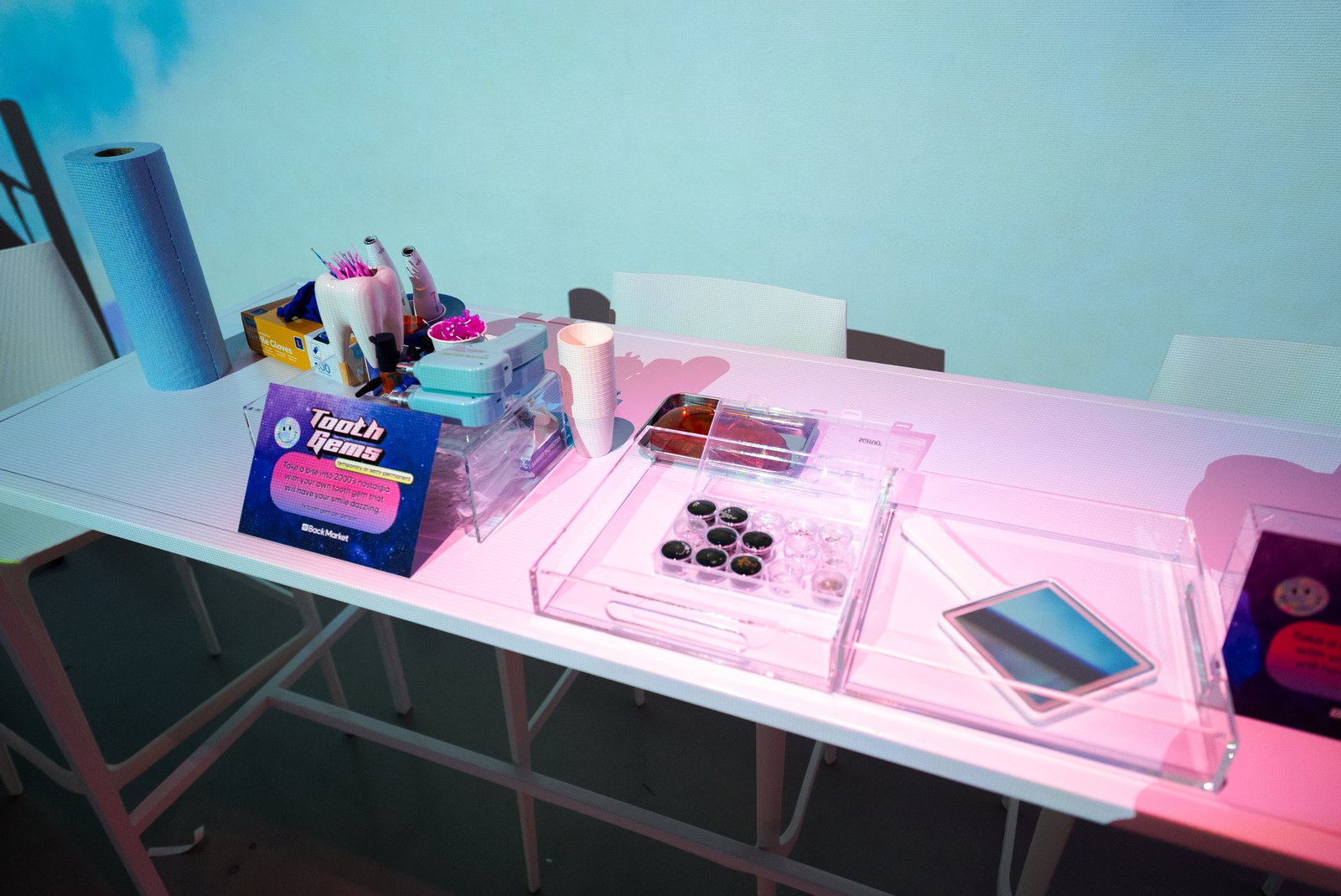 Pink lit table holding acrylic trays, phone parts and tools under blue and pink wash light