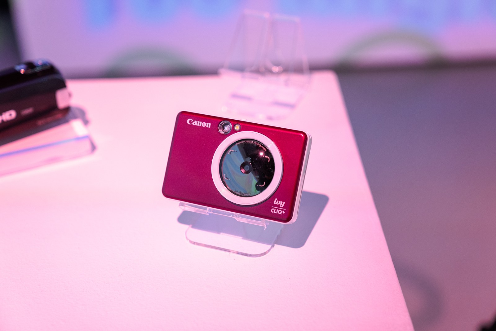 Red Canon instant camera on a clear stand on a pink lit table