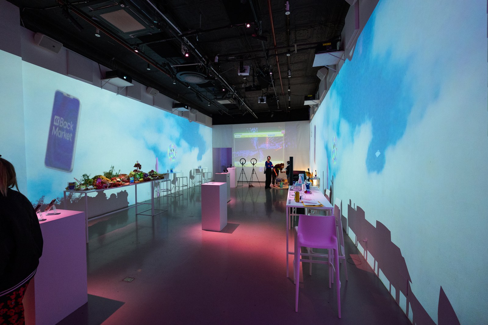 Long white room washed in blue sky projections with a Back Market phone graphic on the wall