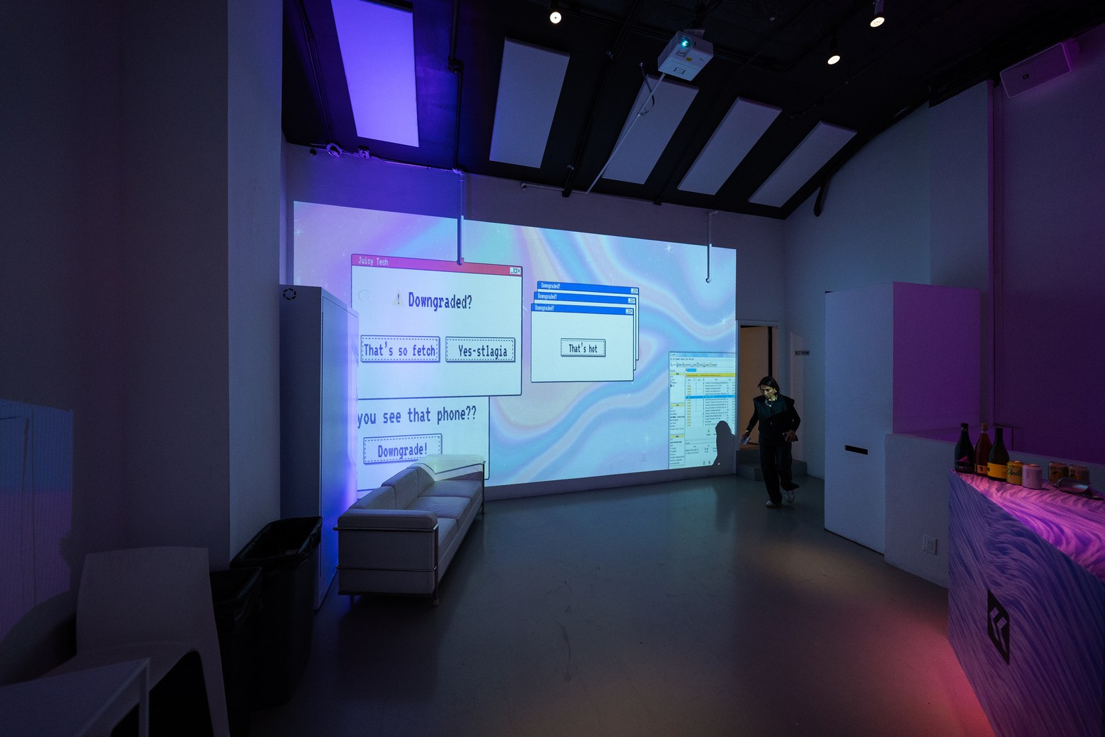 Wall projection of retro dialogue boxes reading Downgrade above a white sofa in a purple lit room