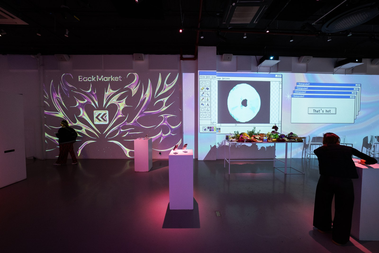 Guests browse a projection lit room with a Back Market logo mural and a retro computer window on the wall
