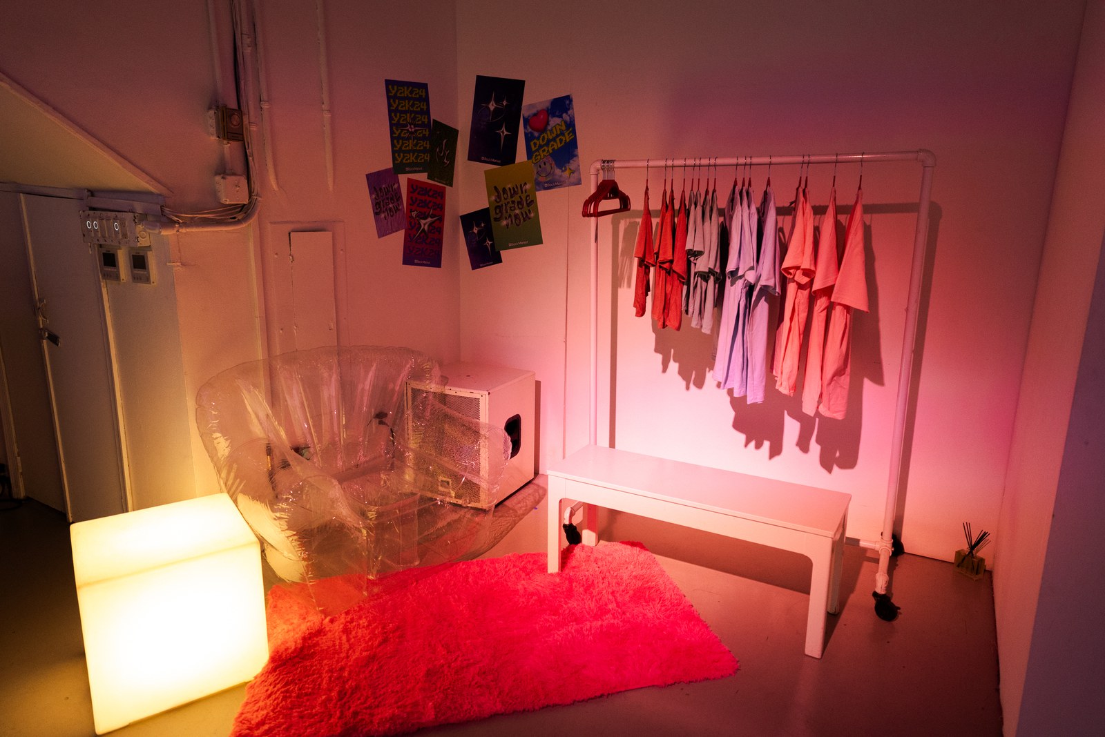 Pink lit corner with posters taped to the wall, a clothes rack, an inflatable chair and a red shag rug
