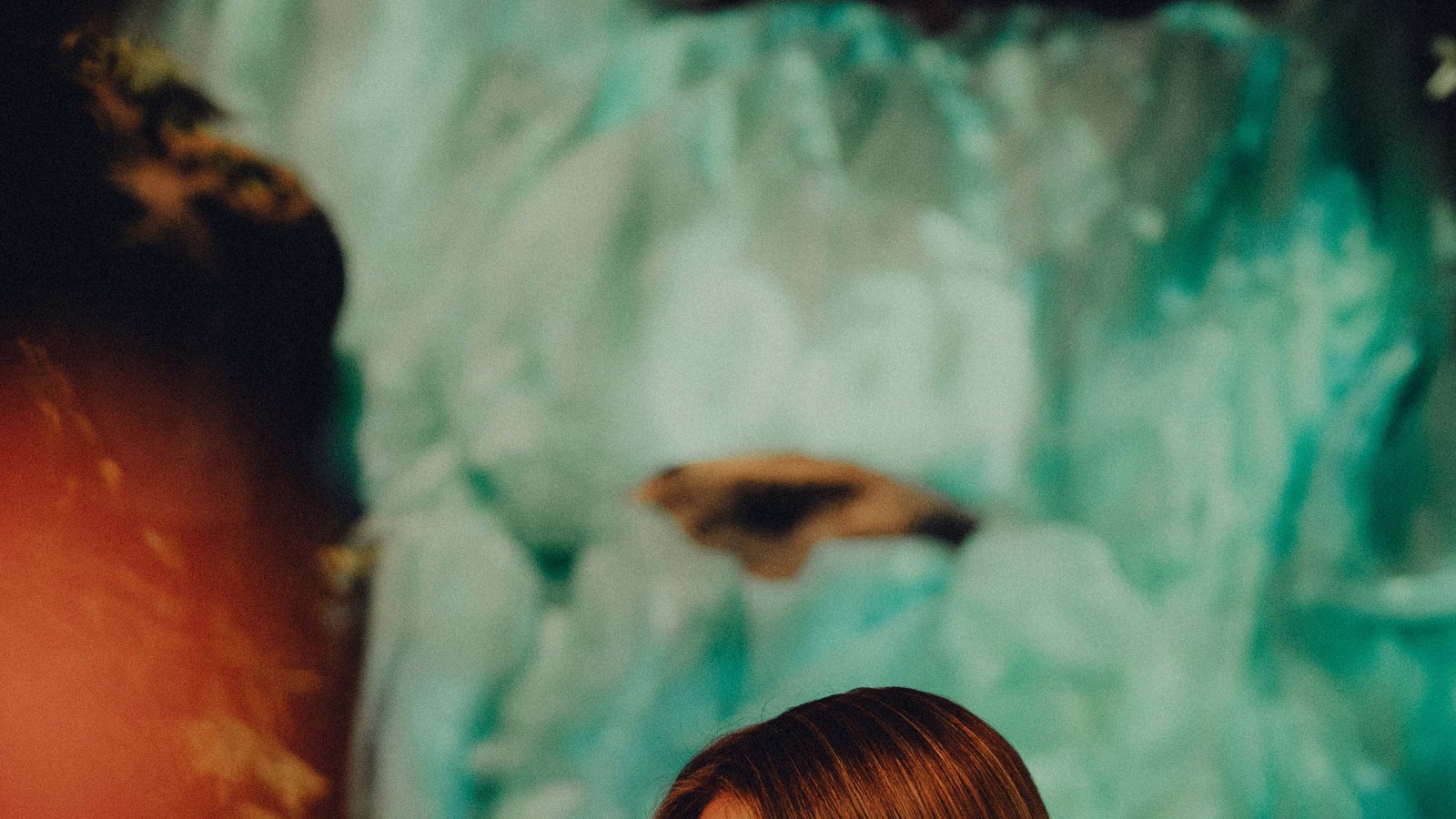 Blurred back of a head against a pale turquoise waterfall set with warm light flaring on the left