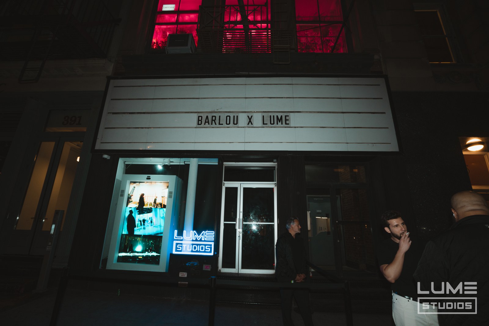 Marquee reading Barlou x Lume above a storefront at night, red lit fire escape overhead and a Lume Studios sign