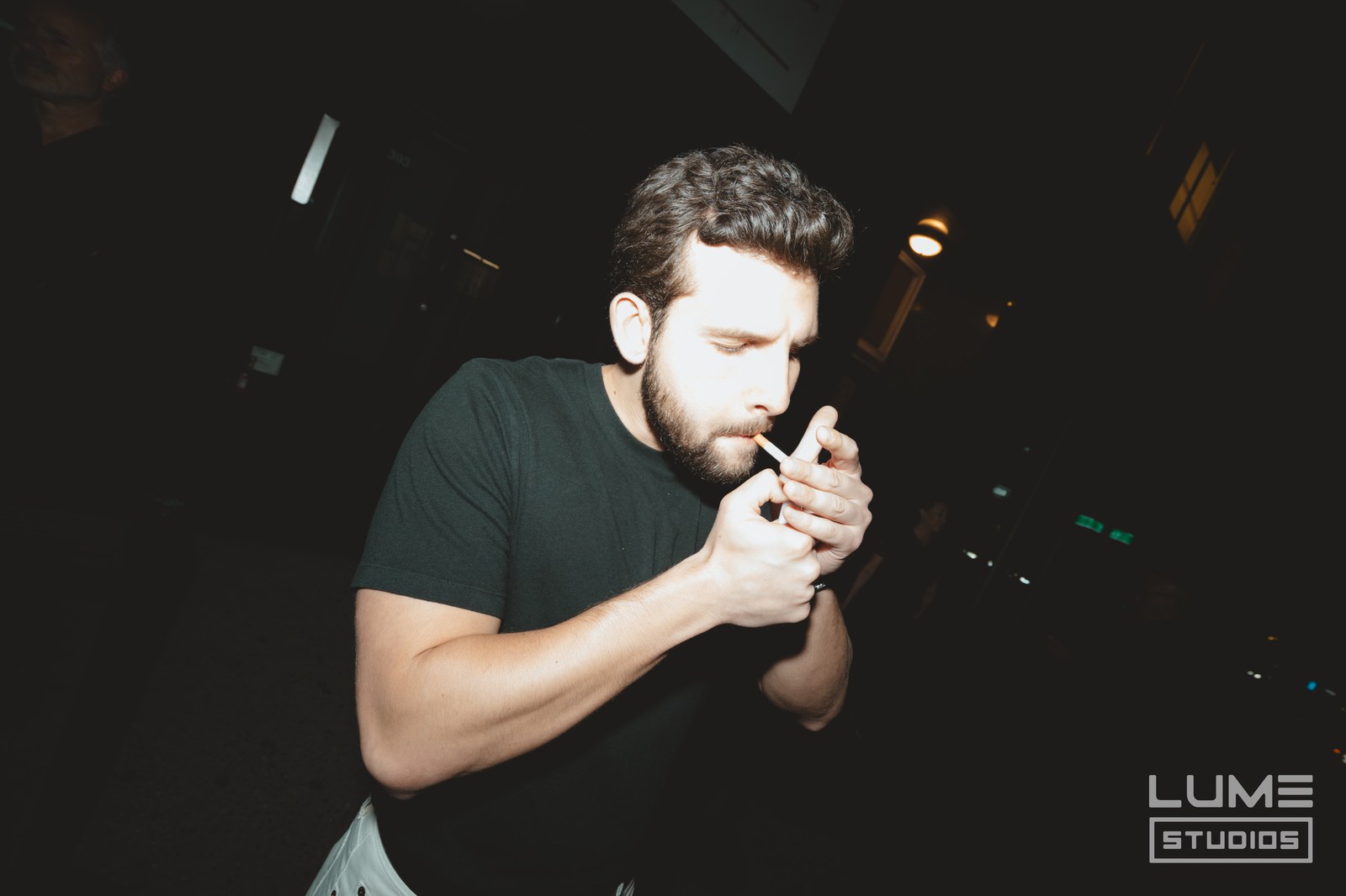 Flash lit man in a black tee lighting a cigarette in a dark club