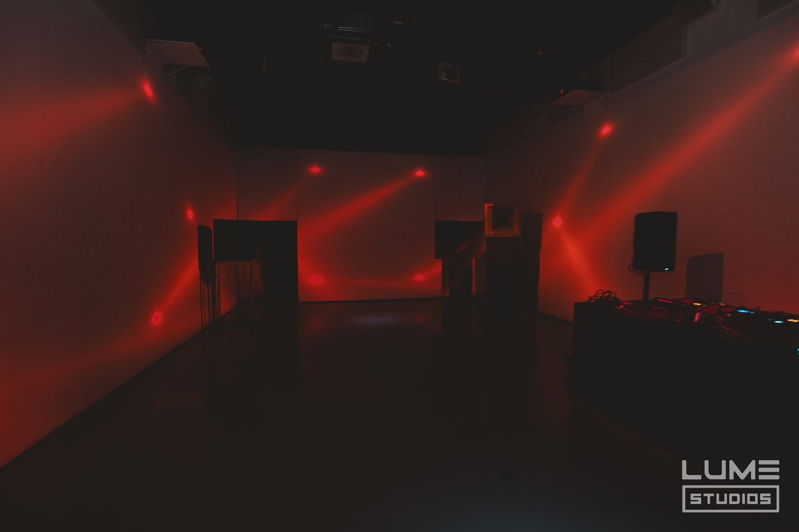 Empty dark studio washed in red light with beams from moving heads hitting the walls and DJ speakers