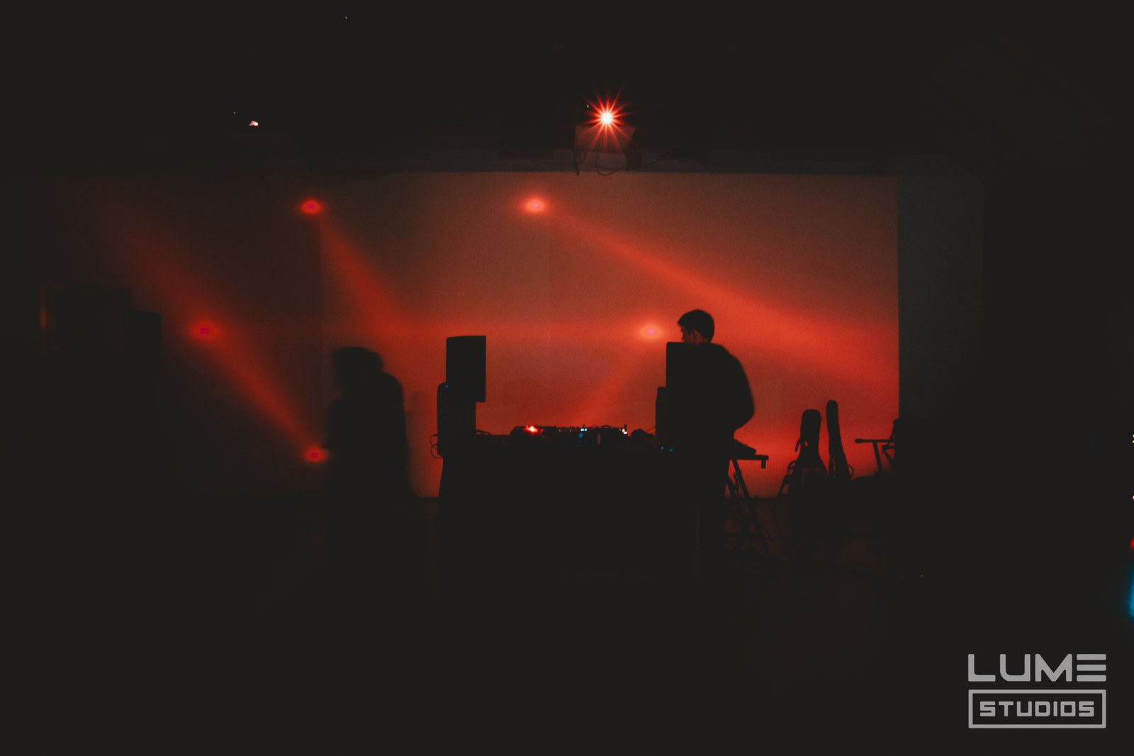 Silhouette of a DJ behind decks against a wall of red haze and crossing red light beams