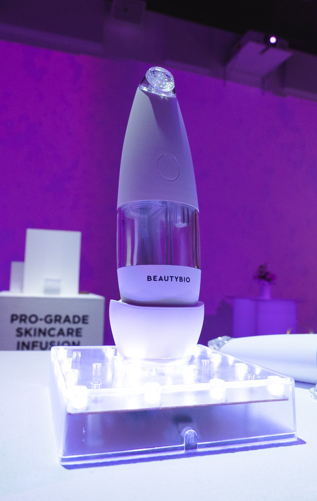 BeautyBio skincare device glowing on a lit pedestal against a purple wall in New York City
