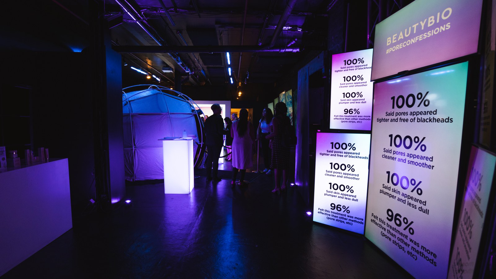 Dark purple lit room with tall BeautyBio panels listing pore statistics beside a glowing white bar