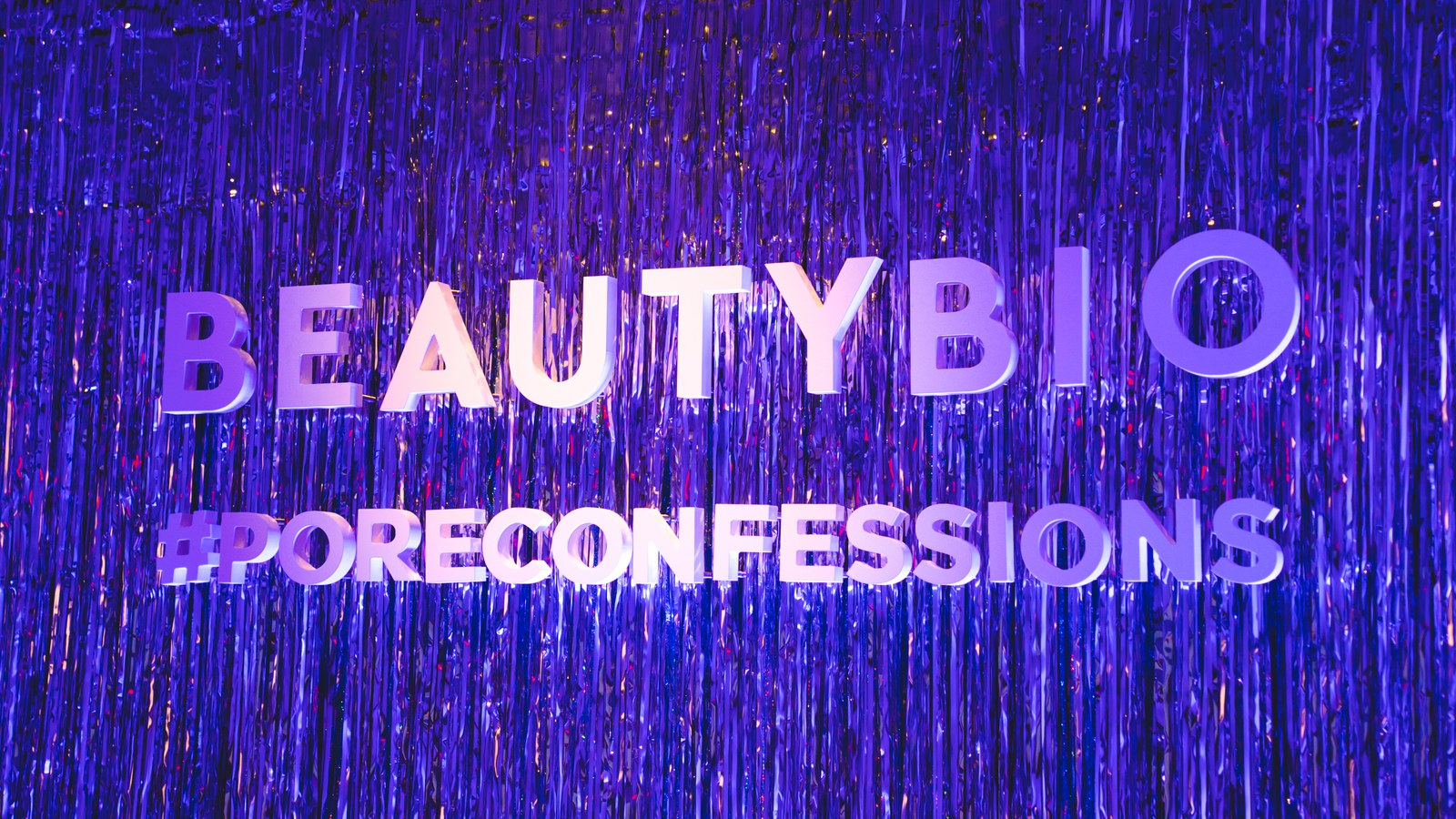 BeautyBio and PoreConfessions letters shine against a shimmering purple foil curtain