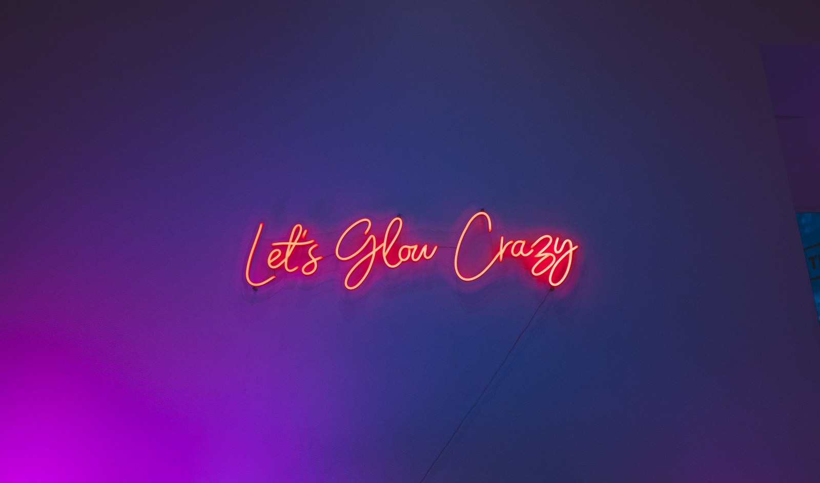A red neon sign reading Let’s Glow Crazy glows on a wall washed in blue and purple light
