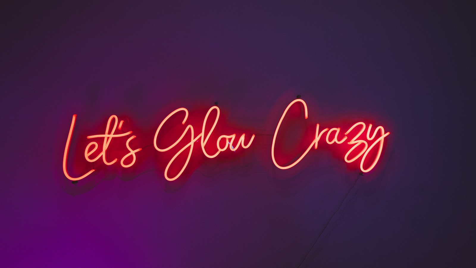Red neon script reading Let’s Glow Crazy glowing against a dark purple wall