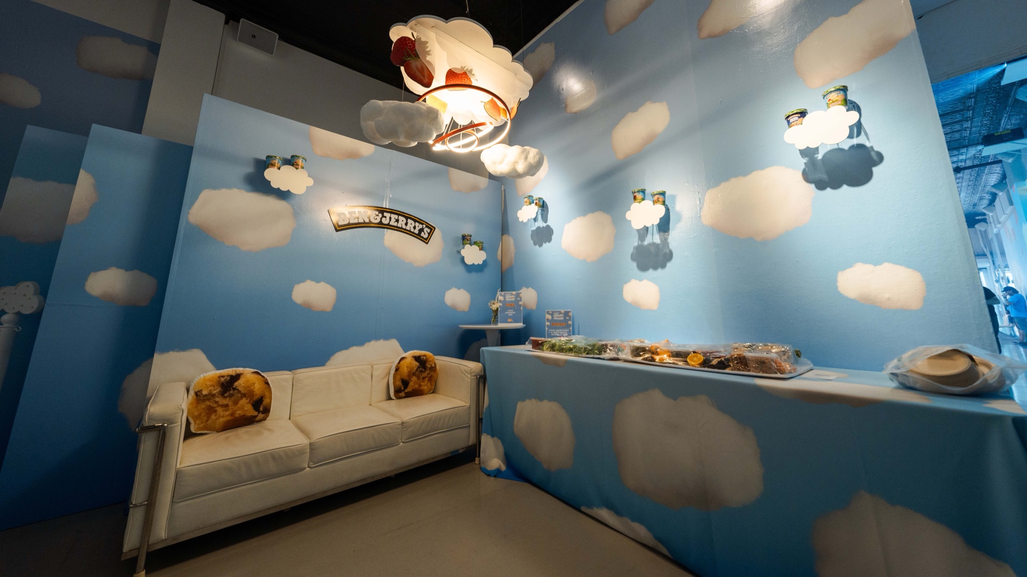 Ben & Jerry’s cloud lounge features white sofa, cookie pillows and dessert table beneath a strawberry lamp