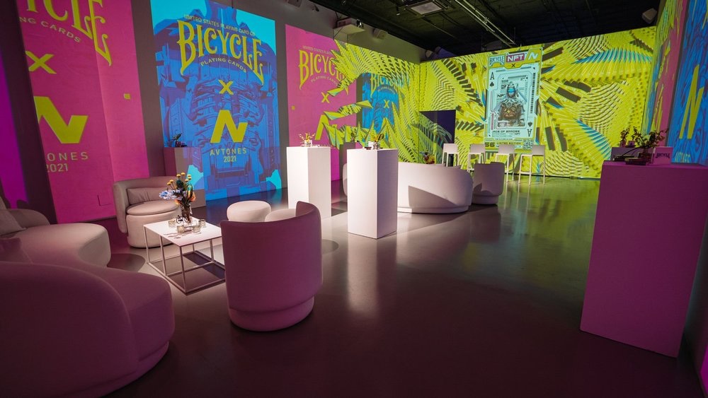 White lounge seating under vivid pink and green Bicycle NFT projections at the unveiling event