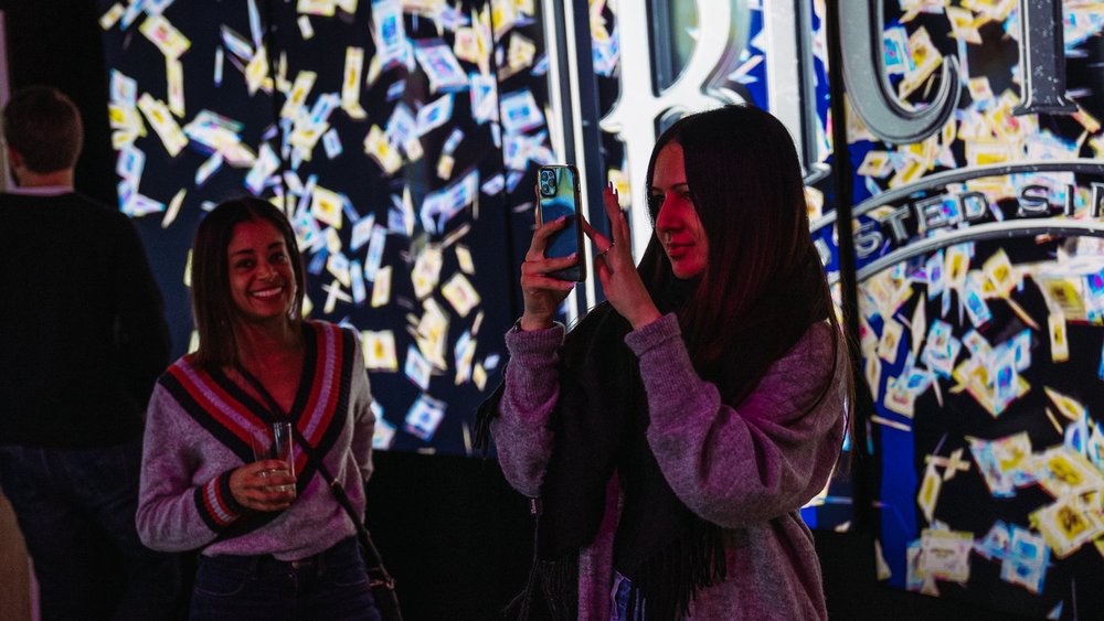 Guest photographs a giant animated Bicycle card wall while a friend smiles nearby