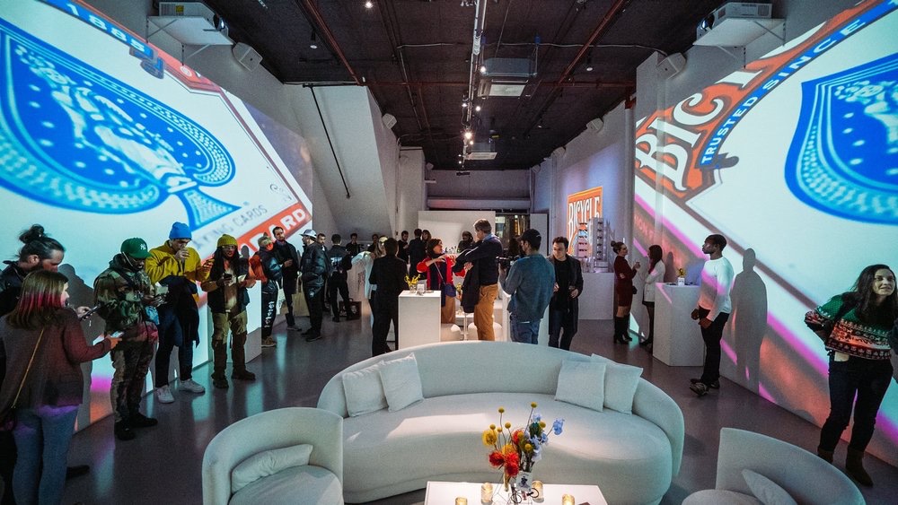 Attendees mingle between towering ace of spades projections at the Bicycle NFT unveiling