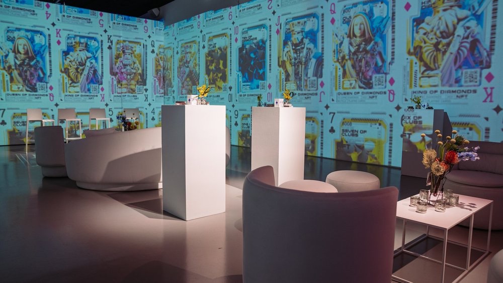 Curved white sofas face walls covered in futuristic Bicycle NFT playing card designs
