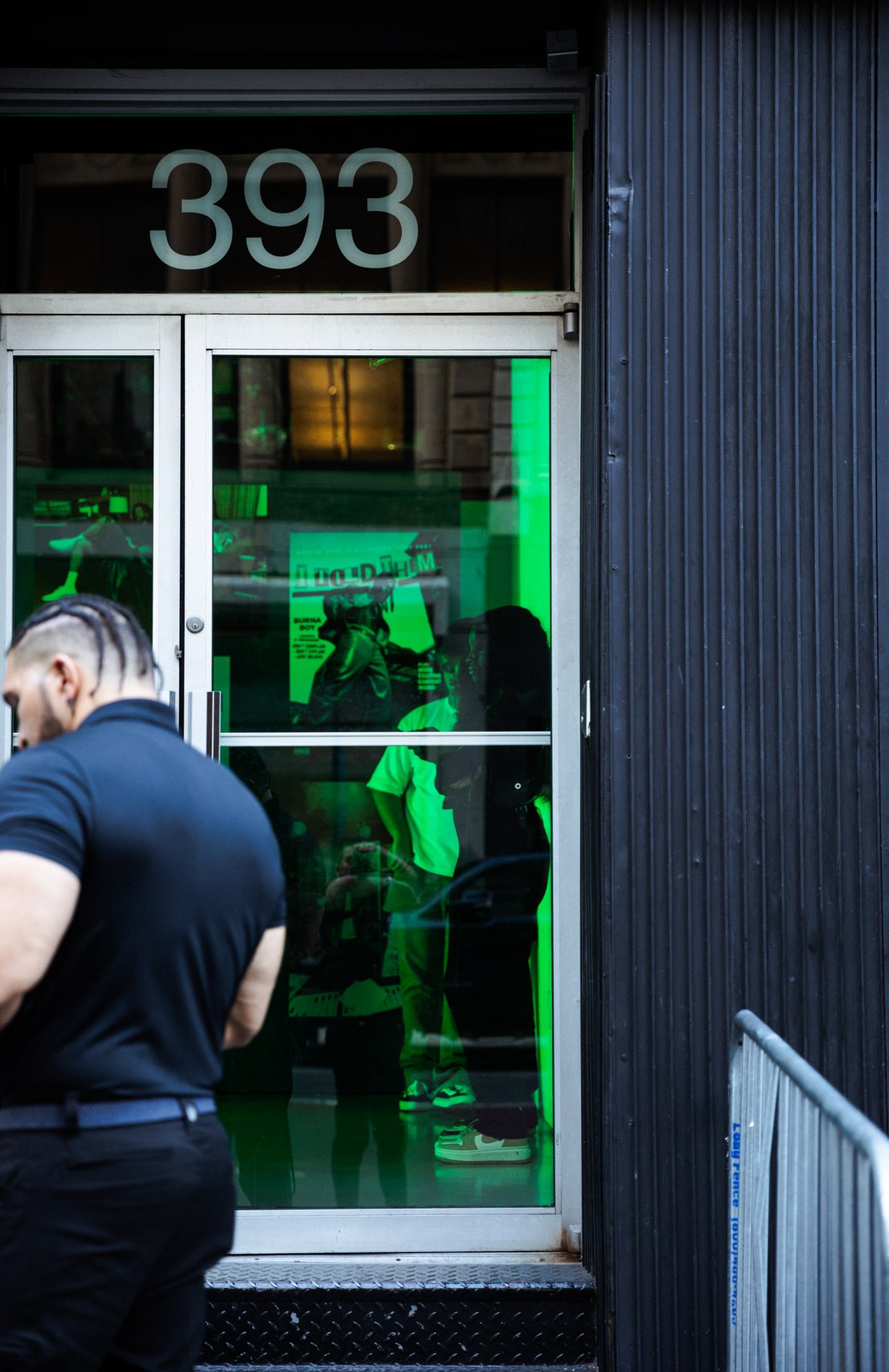 Green lit glass door numbered 393 with silhouettes inside as a man in black walks past
