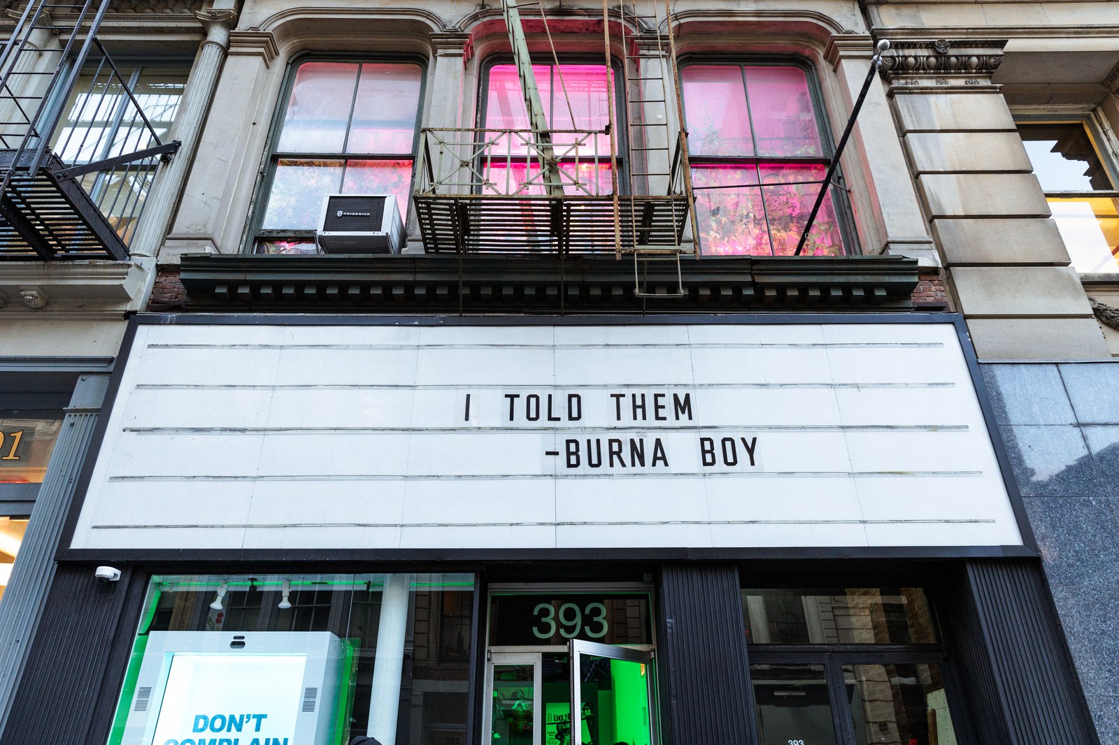 Marquee reading I Told Them, Burna Boy above a doorway numbered 393, pink lit windows on the floor above