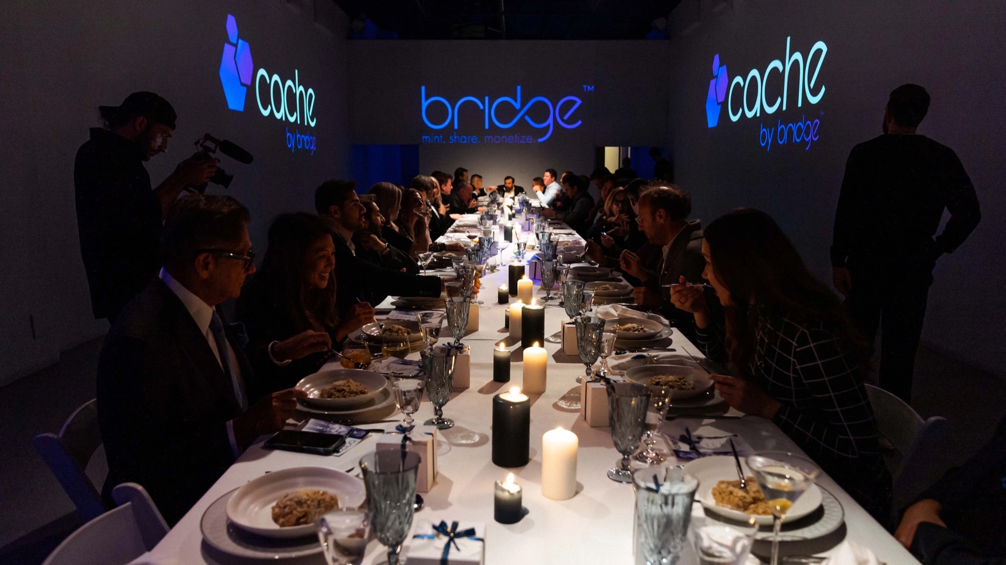 Guests dine along a candlelit table while Cache and Bridge logos glow on the walls of Lume Studios