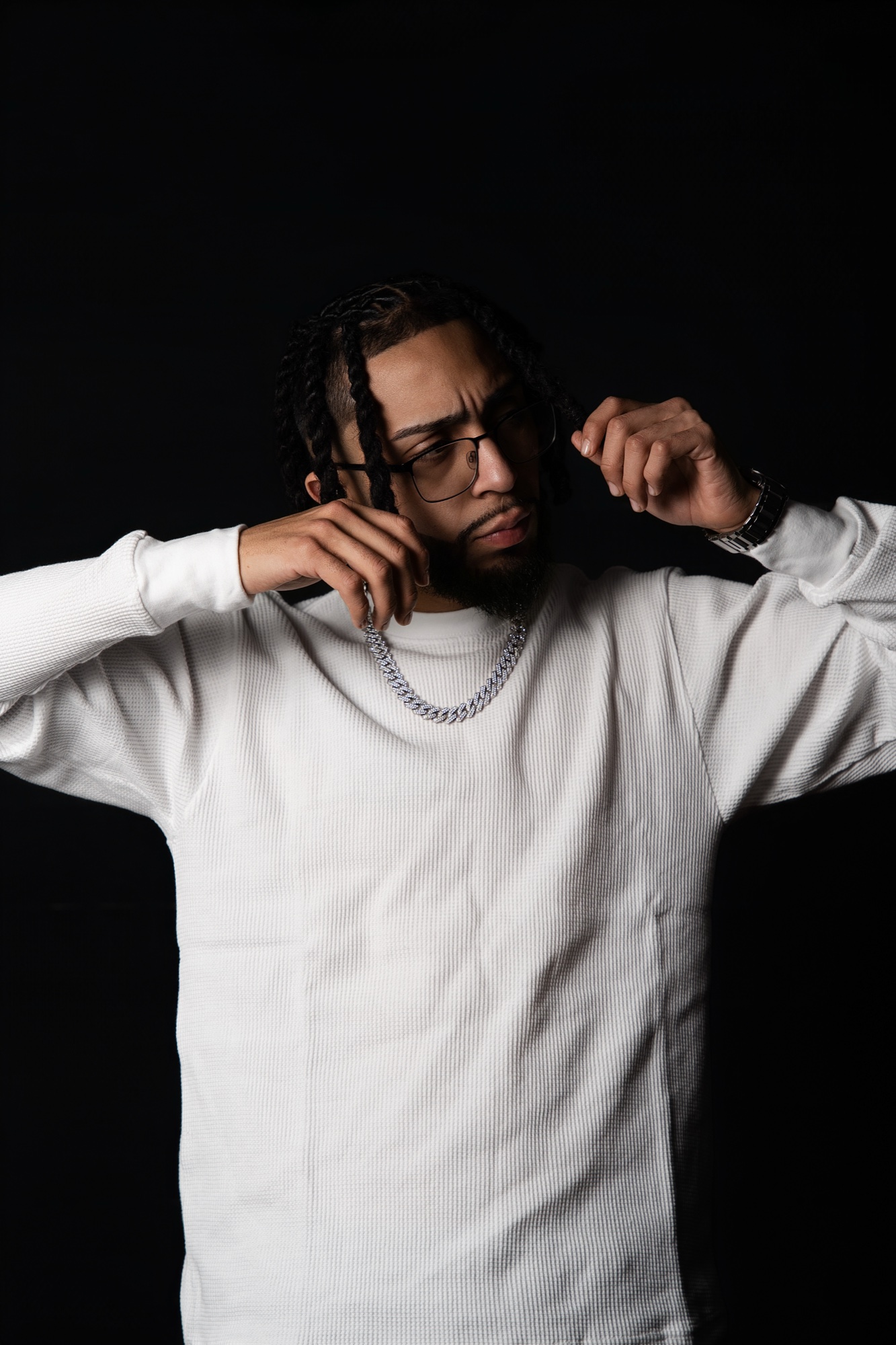 ThePlug Dino in a white waffle knit top and silver chain, both arms raised, looking down