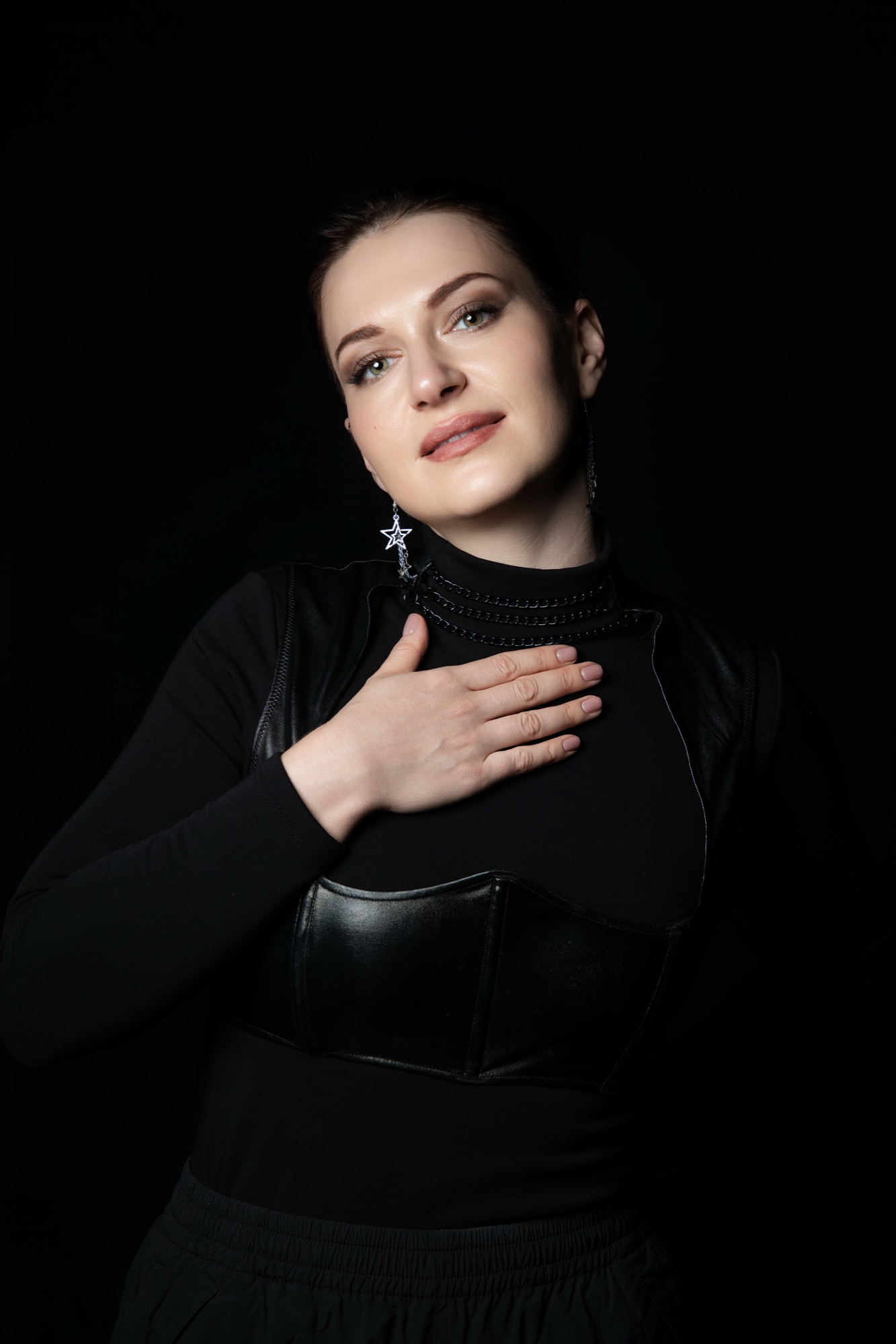 Nadia Kodes with one hand flat on her chest, black top and leather bodice, star earring
