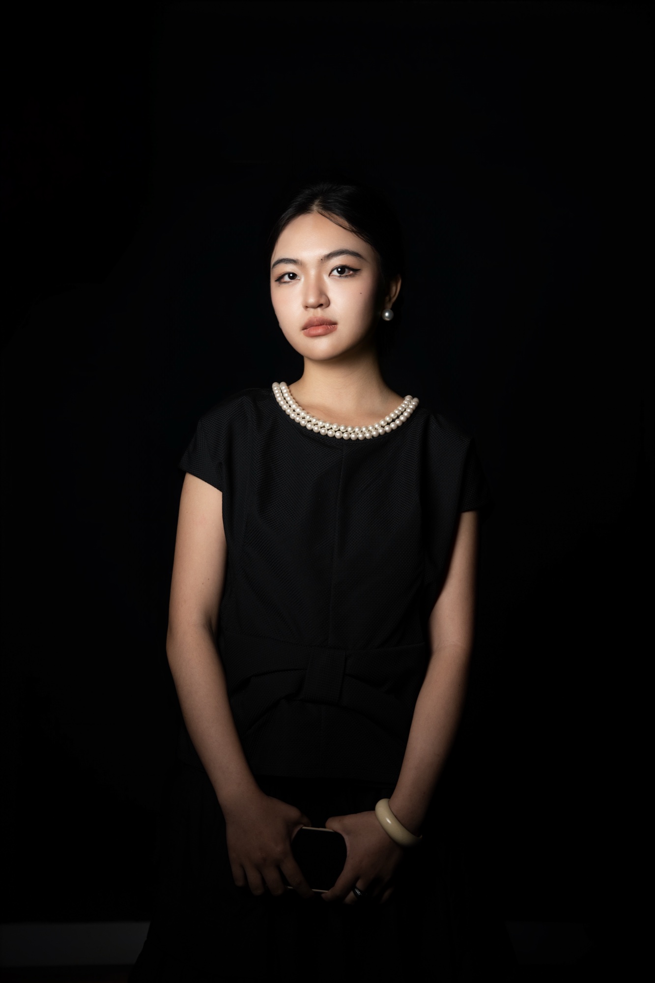 April in a black top and pearl necklace, hands clasped in front, looking at the camera