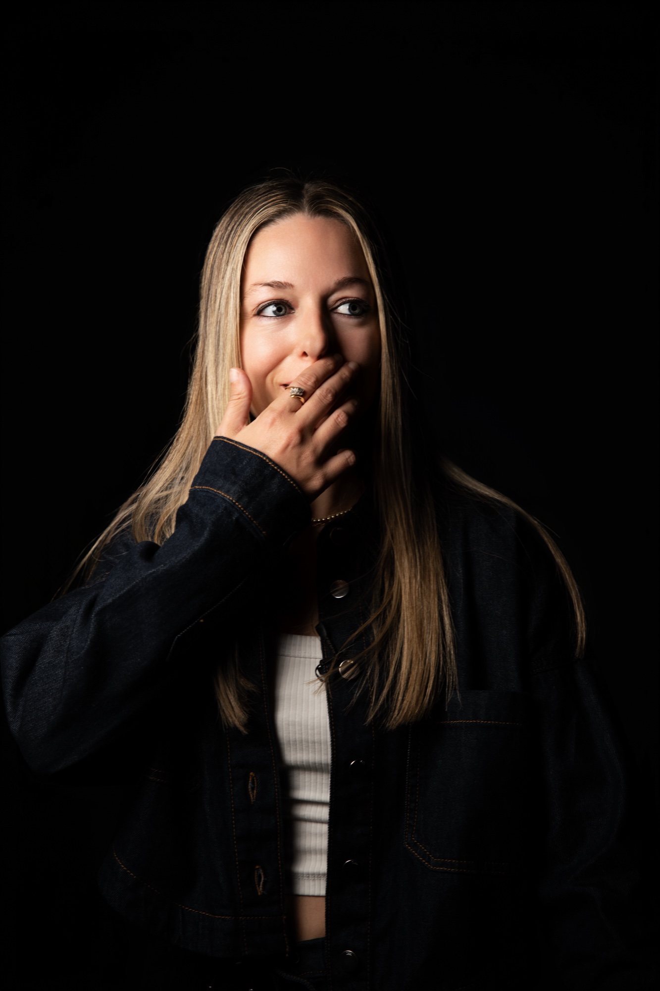 Shay Mizz with one hand over her mouth, denim jacket over a white ribbed top