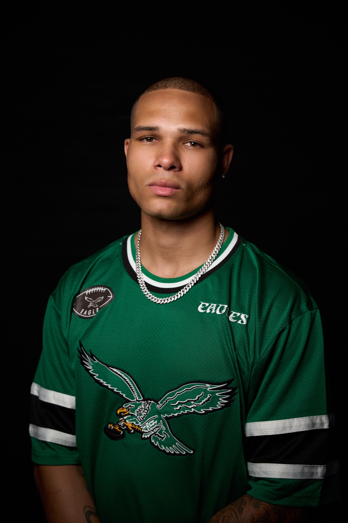JENSN in a green Eagles jersey with a silver chain, looking straight into the camera