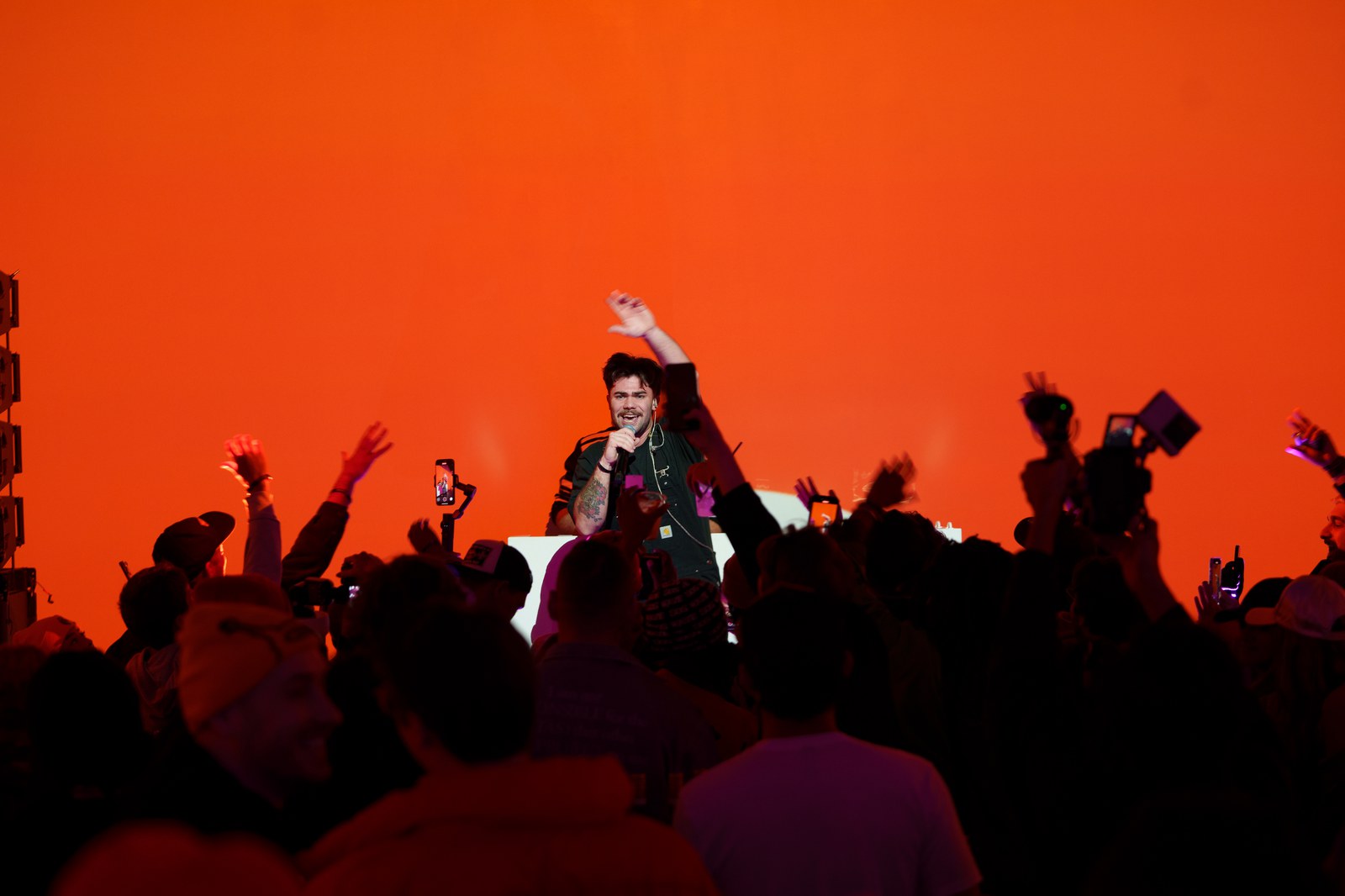 Performer sings into a mic before a glowing orange wall as the Cashear Launch Party crowd raises hands