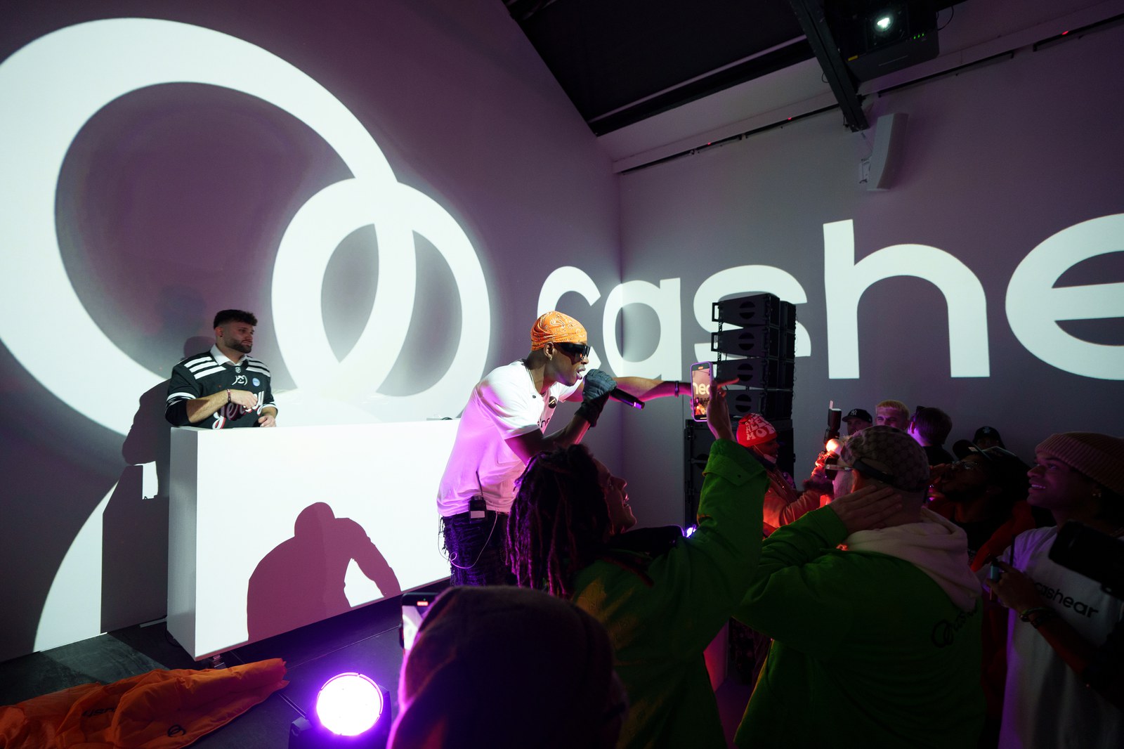 A performer behind a lit console in front of the illuminated Cashear wordmark, guests silhouetted at the edge