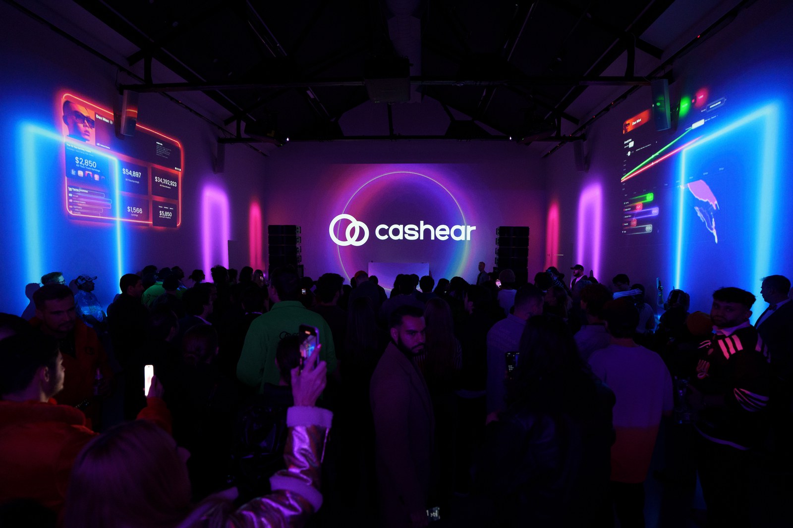 A crowd faces a Cashear logo on a projection wall framed by neon pink and blue light columns