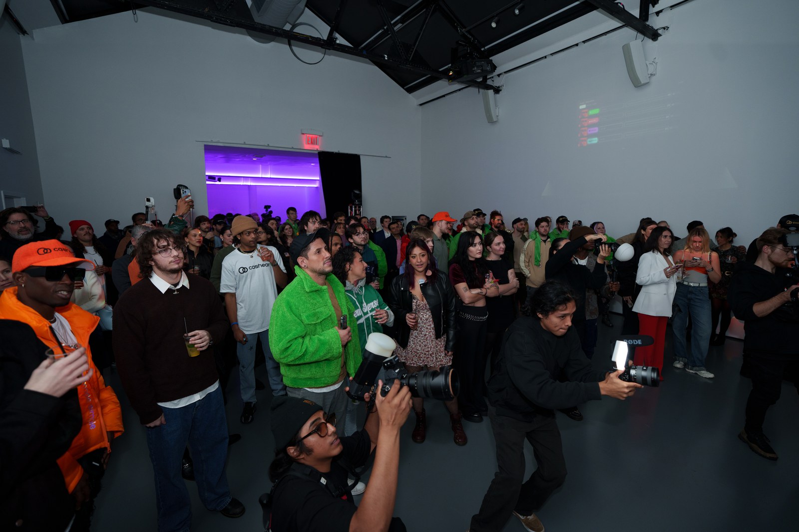 Guests in a white gallery space look toward the camera as a photographer kneels in the foreground