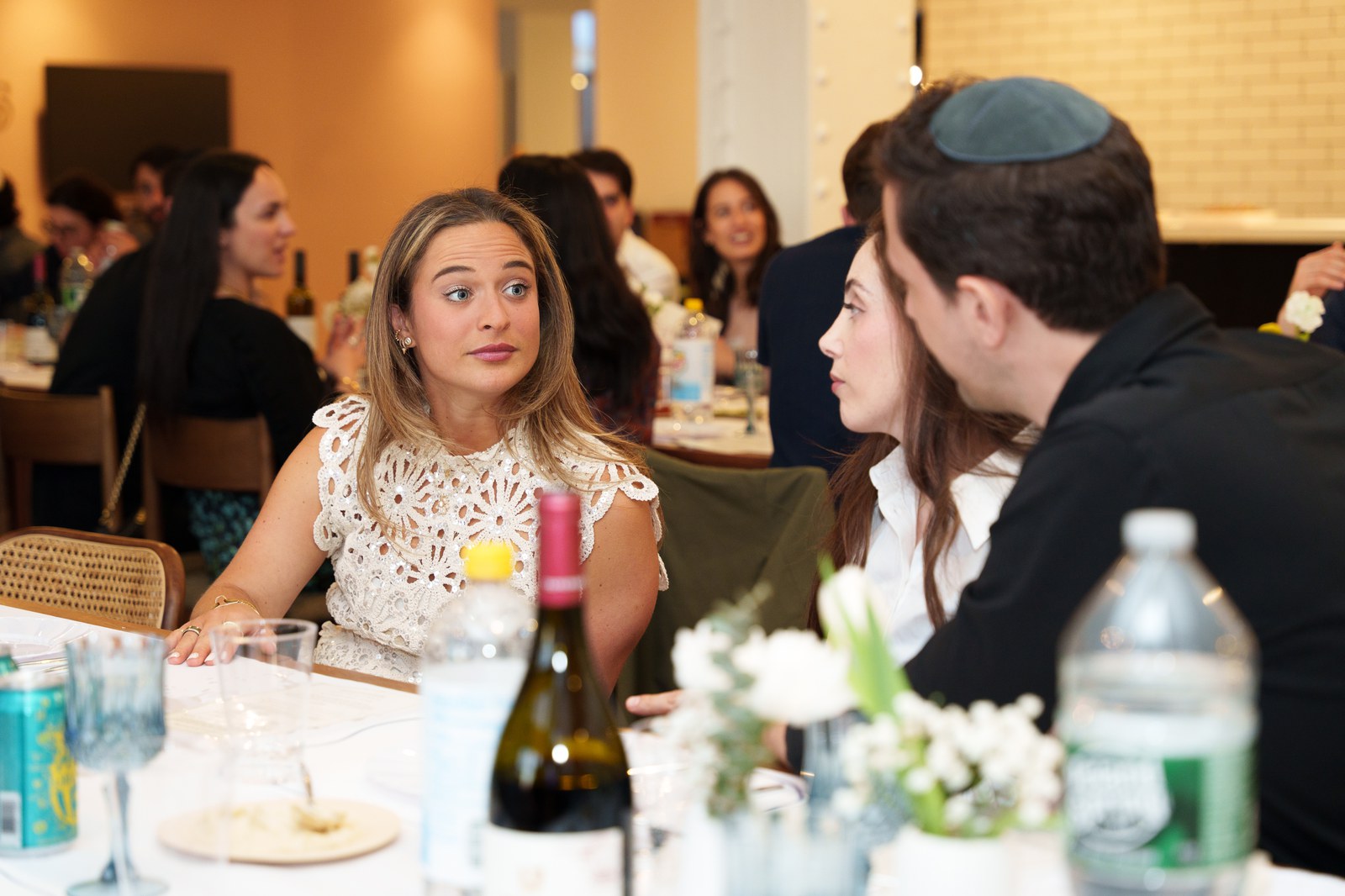 Guests around a laid table in a warm room, one looking back toward the camera mid conversation
