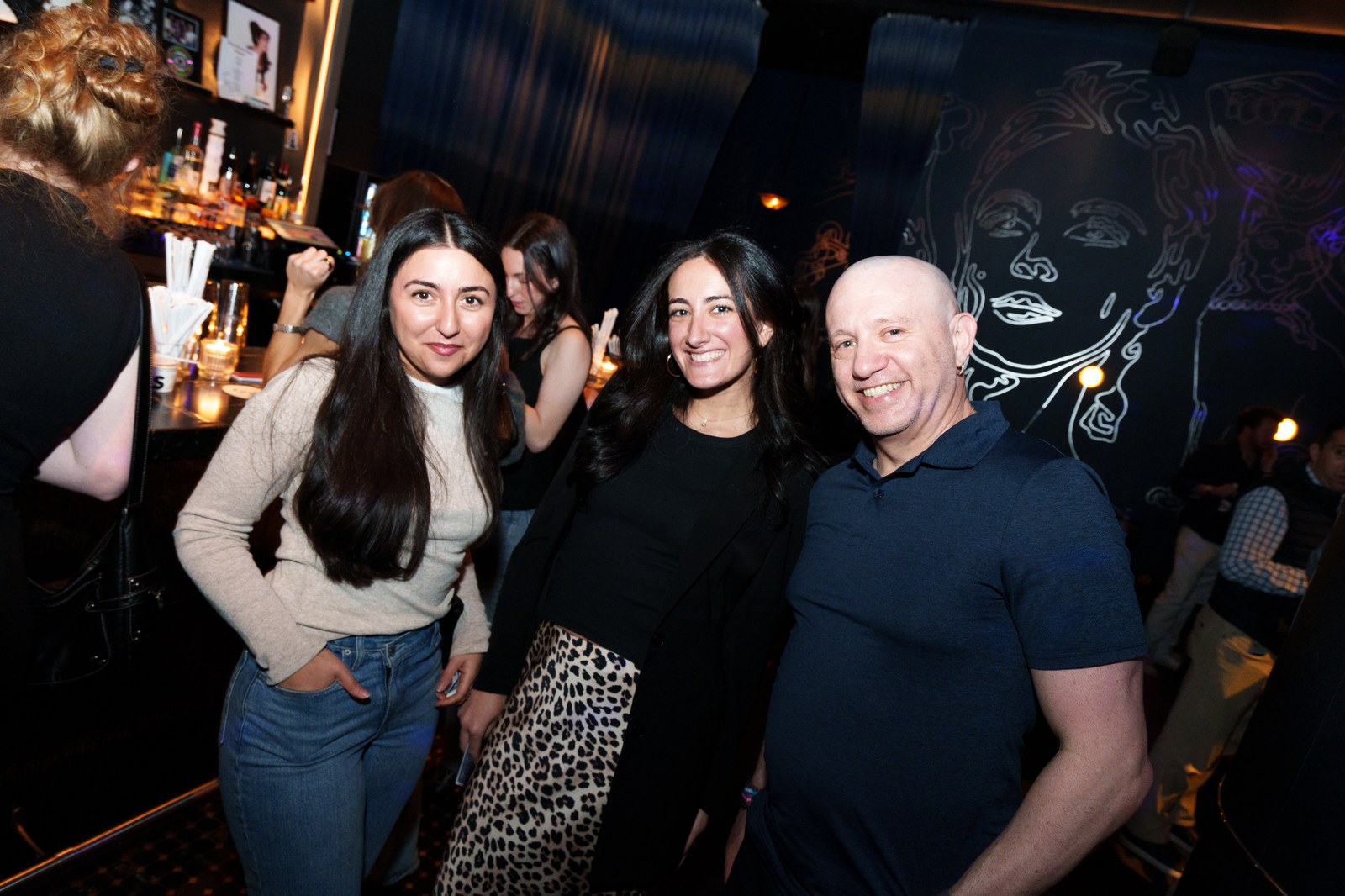 Three guests standing together at the bar later in the evening under low light