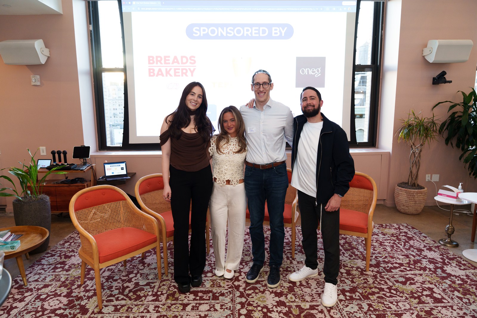 Four people pose on a patterned rug in front of a screen reading sponsored by with Breads Bakery logo
