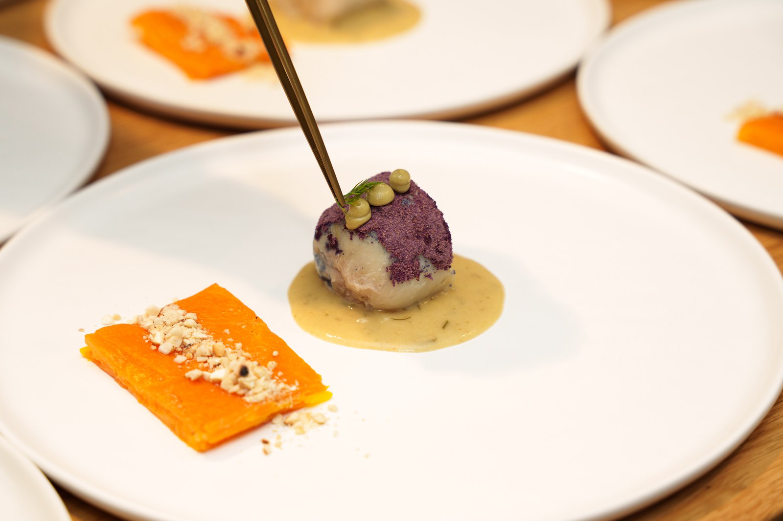 A purple cauliflower floret in pale sauce beside a slab of orange squash on a white plate, a spoon above