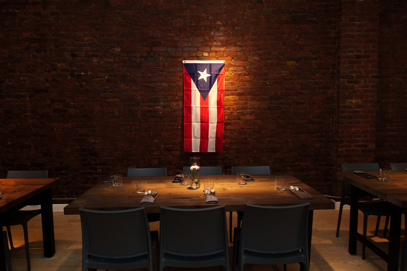 Puerto Rican flag hung on an exposed brick wall above a dark wooden dining table with grey chairs