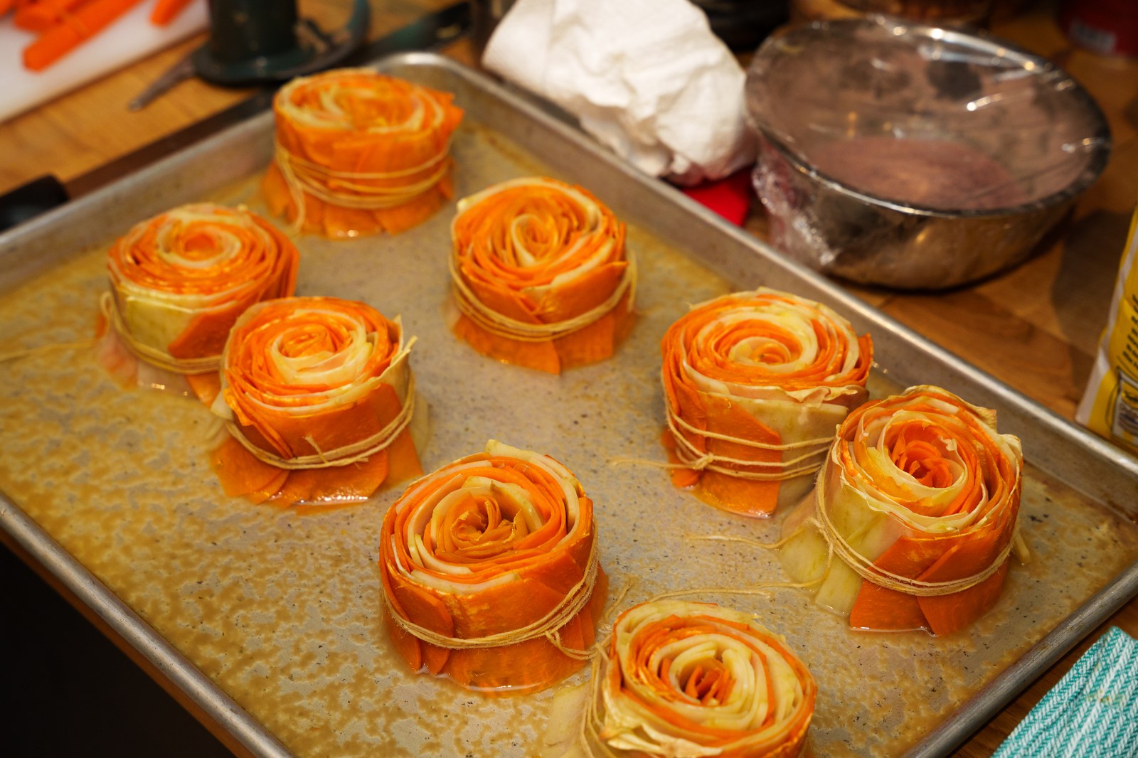 Eight rolled spirals of orange and yellow vegetable ribbons tied with string on an oiled sheet pan
