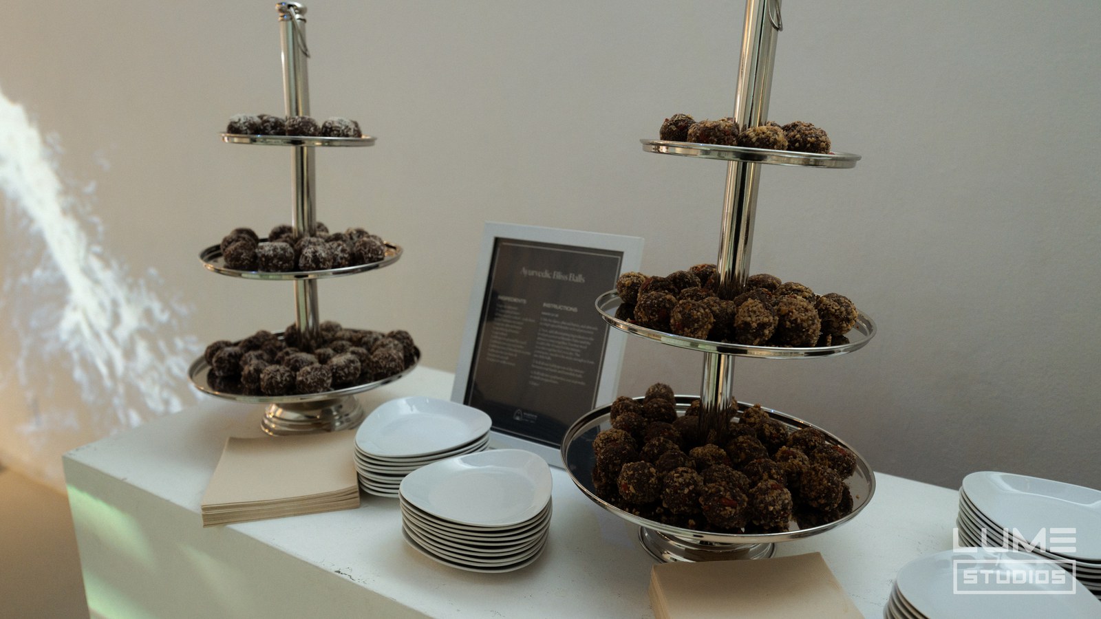Two tiered silver stands of chocolate truffles beside stacked white plates and a small printed menu card