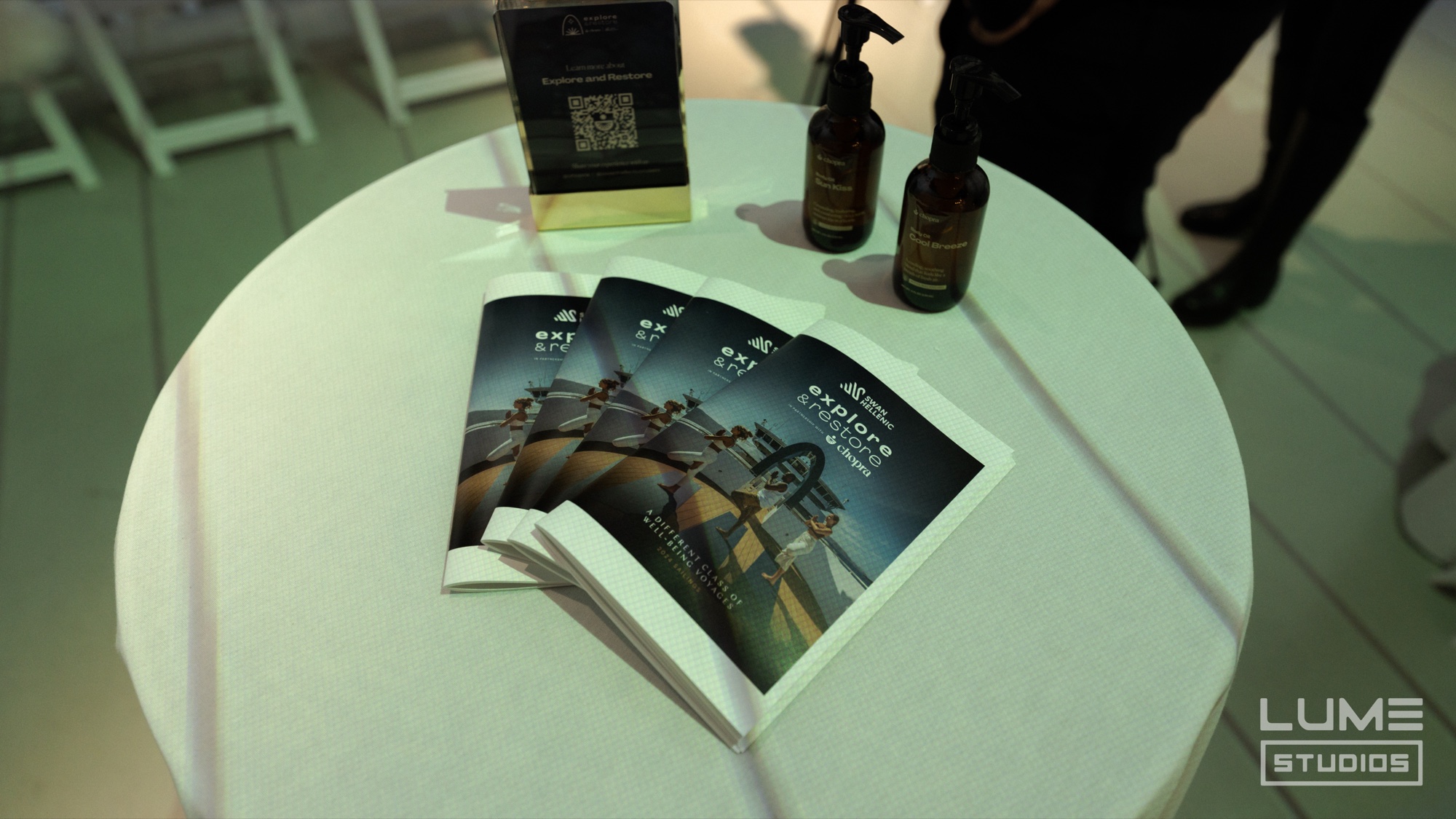 Overhead view of a round white table with fanned brochures, amber pump bottles and a QR code stand