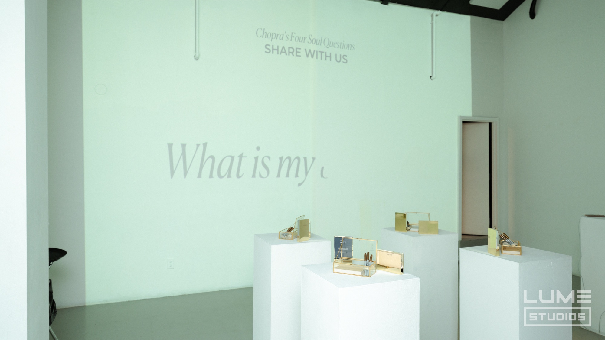 Pale green room with the words What is my projected on the wall above white plinths of small product boxes
