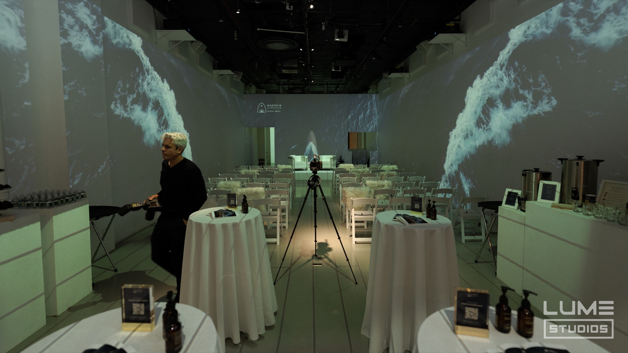 White chairs and round tables set for a talk between walls projected with crashing ocean waves