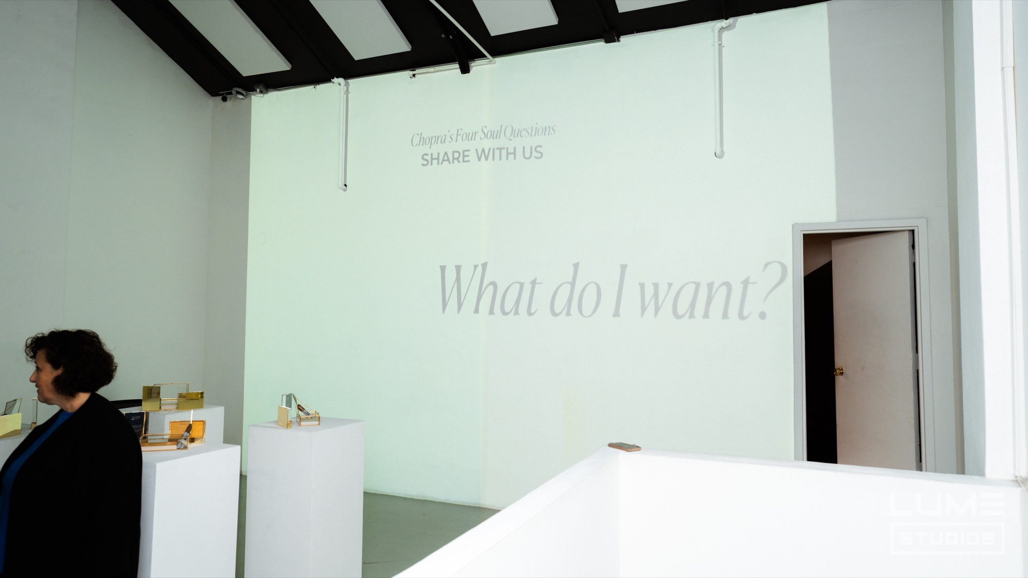 White gallery wall with the projected words What do I want above small product plinths and an open doorway